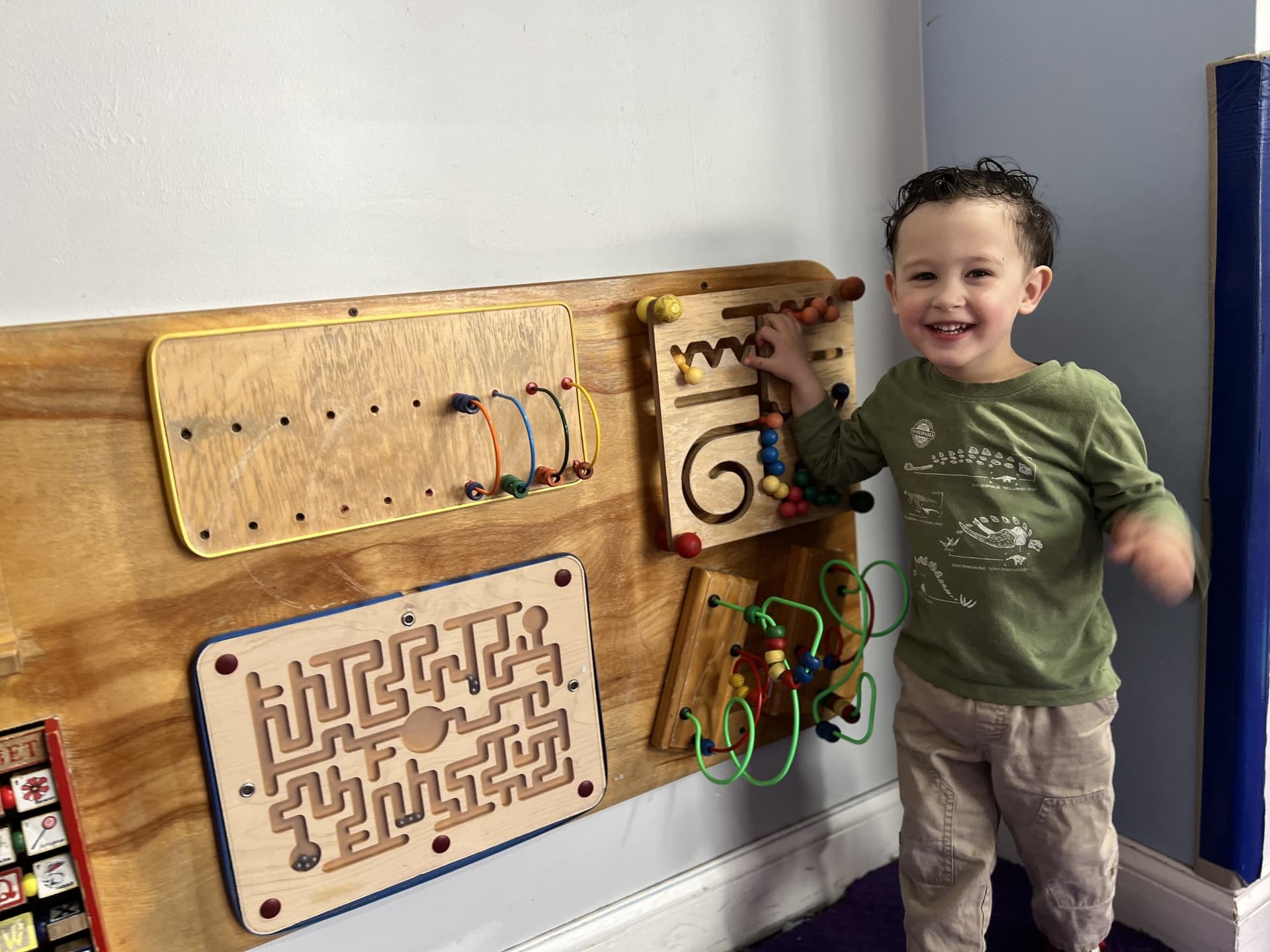 A child playing at a wooden sensory activity wall in a Creation Kingdom classroom