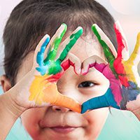Preschool child making heart with painted hands.